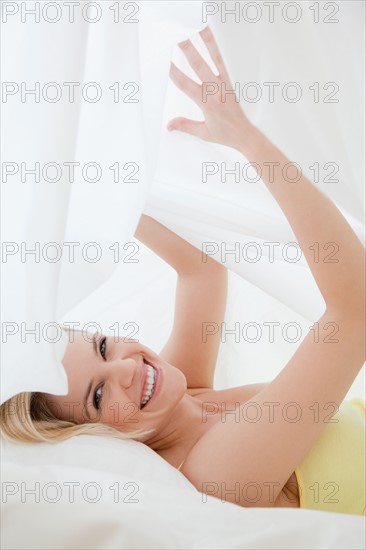 Blonde woman hiding under bed sheet. Photo : Jamie Grill