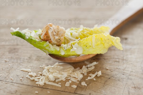 Fresh caesar salad on wooden spoon.