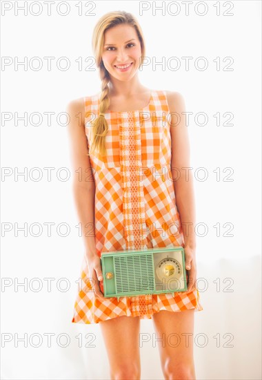 Studio portrait of young woman holding antique radio.