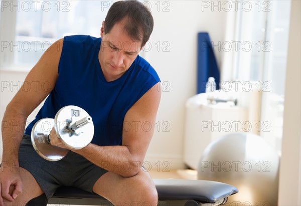 Mature man lifting weights in gym.