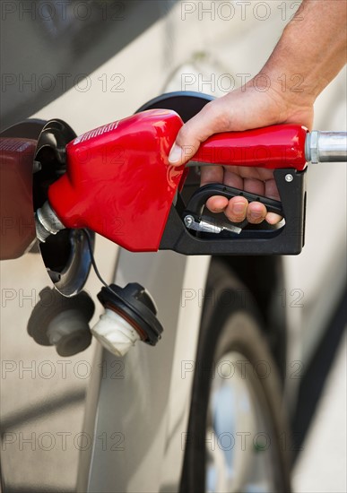 Hand holding fuel pump refueling car.