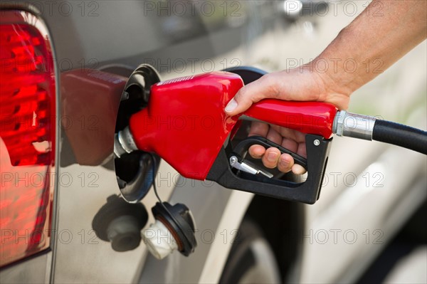 Hand holding fuel pump refueling car.