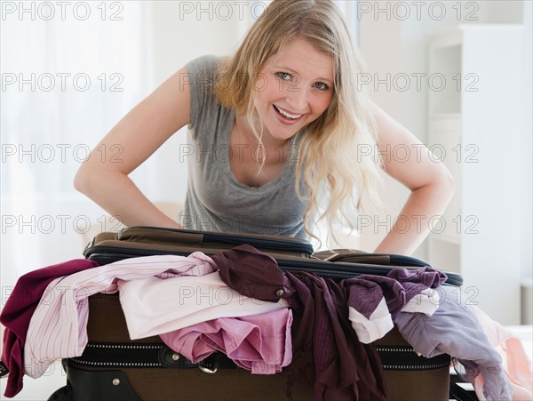 young woman trying to close luggage. Photo : Jamie Grill