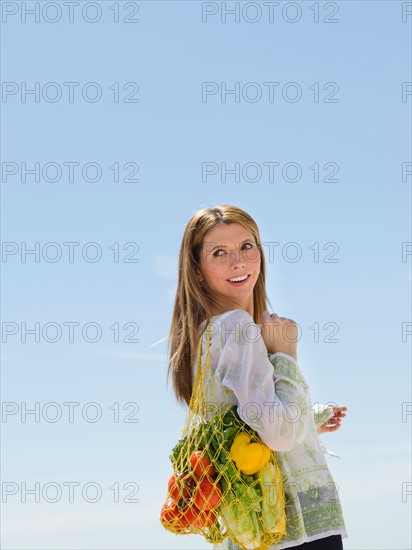 Woman carrying net bag of fruit and vegetables outdoors.