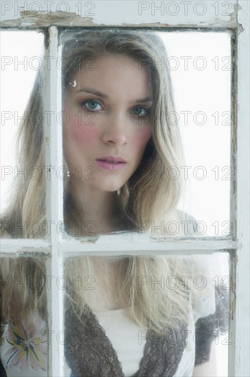 Portrait of young woman looking through window.