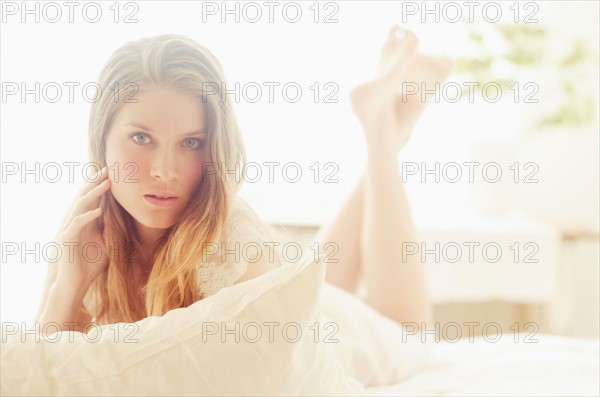 Studio portrait of young woman lying on bed.