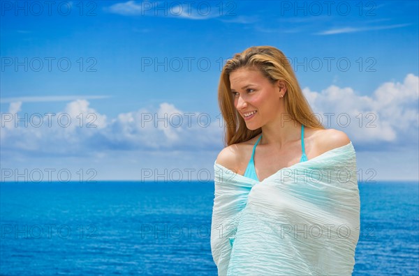 Woman wrapped in towel by sea.