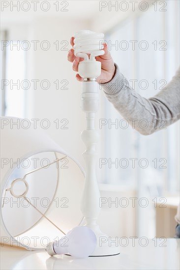 Woman changing classic bulb to energy efficient bulb. Photo : Jamie Grill