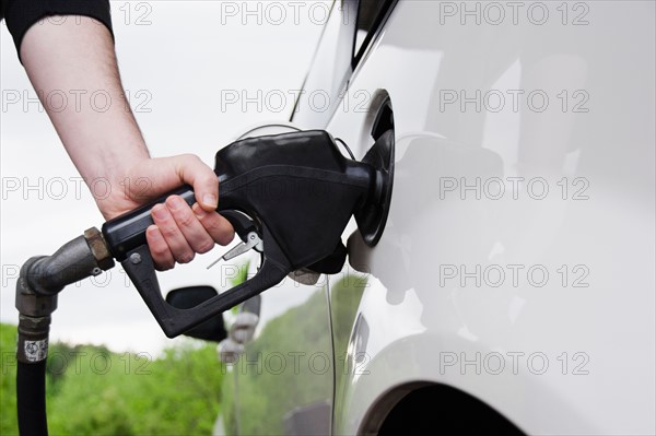 Close up of man's hand holding fuel pump and refueling car. Photo : Jamie Grill