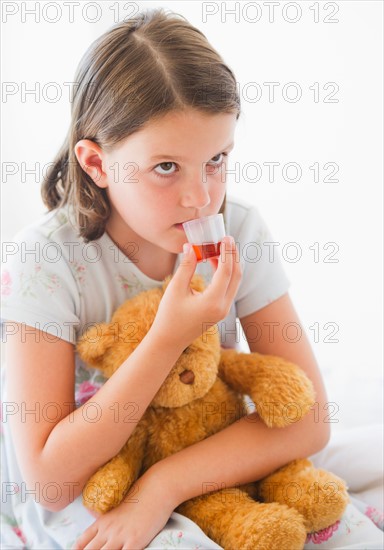 Close up of sick girl (6-7) with teddy bear drinking medicament. Photo: Daniel Grill