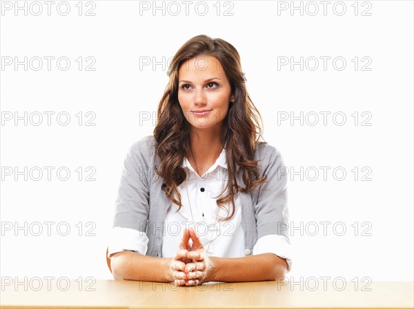Smiling business woman sitting at table with hands clasped. Photo: momentimages