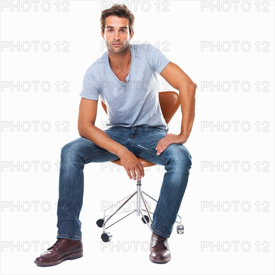 Studio shot of smart young man sitting on chair. Photo : momentimages