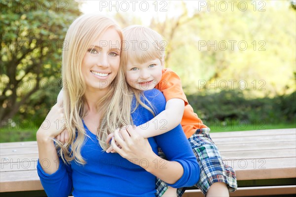 Portrait of mother and son (2-3) sitting at bench in park. Photo : Take A Pix Media