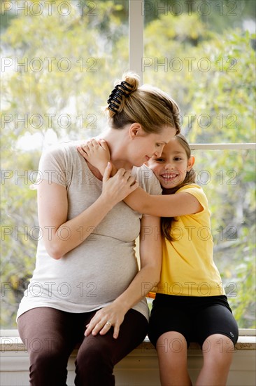 Daughter (6-7) sitting next to pregnant mother, embracing. Photo : Rob Lewine