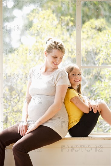 Daughter (6-7) sitting back to back with pregnant mother, embracing. Photo: Rob Lewine