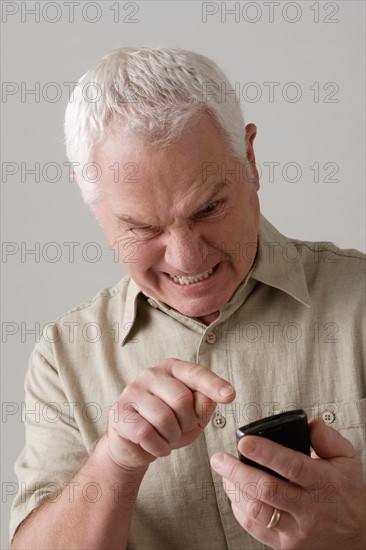 Portrait of angry senior man with mobile phone, studio shot. Photo: Rob Lewine