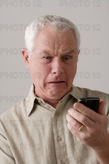 Portrait of senior man with mobile phone, studio shot. Photo : Rob Lewine