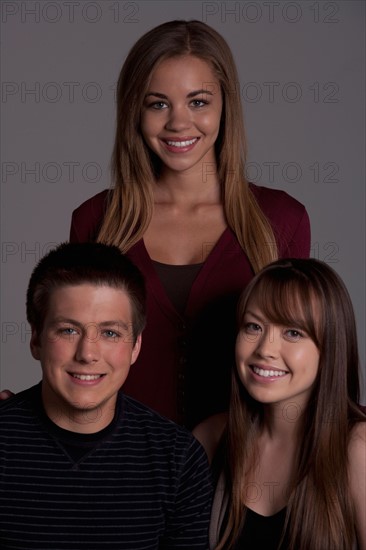 Portrait of teenage boy (16-17) and girl (16-17) with young friend, studio shot. Photo : Rob Lewine