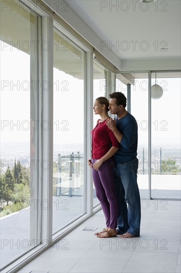 Mature couple in empty living room looking through window. Photo : Rob Lewine