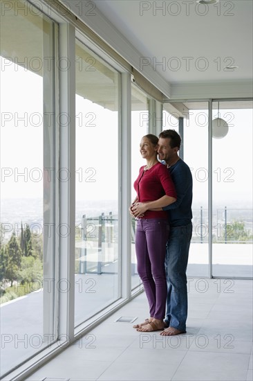 Mature couple in empty living room looking through window. Photo : Rob Lewine