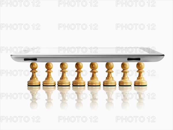 Digital tablet on wooden chess pawns, studio shot. Photo : David Arky