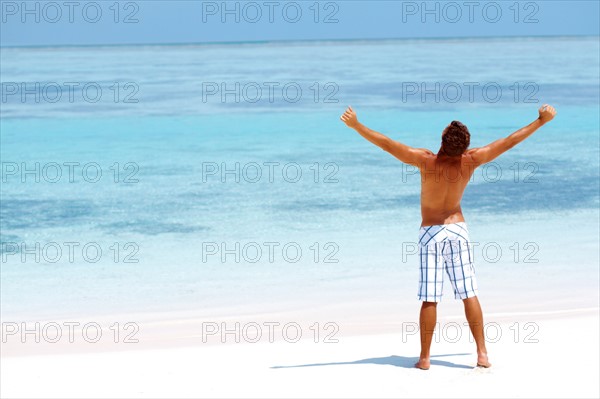 Man standing with his arms wide open on beach. Photo : momentimages