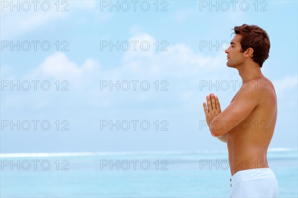 Smart young guy practicing yoga at beach. Photo: momentimages
