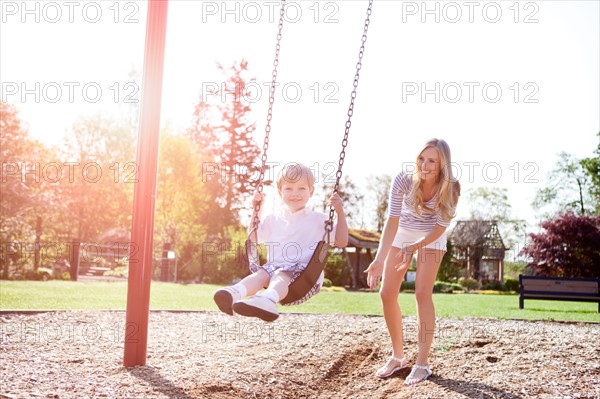 USA, Washington State, Seattle, Mother and son (2-3) swinging on swing in park. Photo : Take A Pix Media