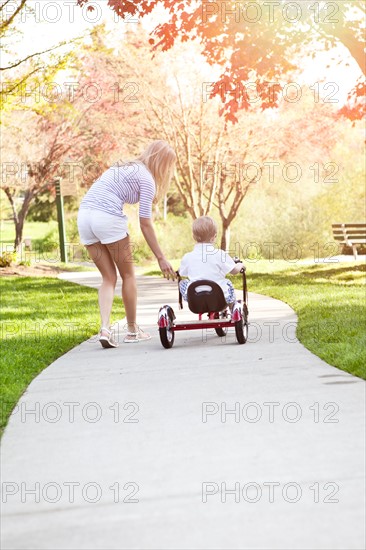 Mother and son (2-3) riding tricycle in park. Photo: Take A Pix Media