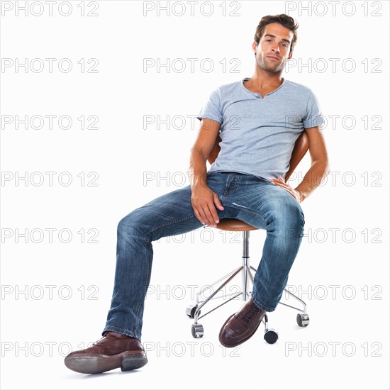 Studio shot of handsome young man sitting comfortably on chair. Photo: momentimages