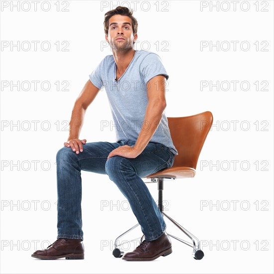 Studio shot of young man sitting on chair with hands on laps. Photo: momentimages