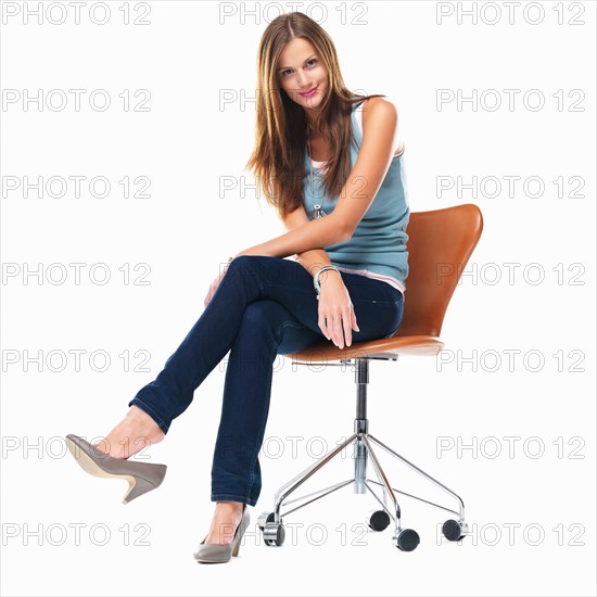 Studio shot of young woman sitting on chair with legs crossed. Photo: momentimages