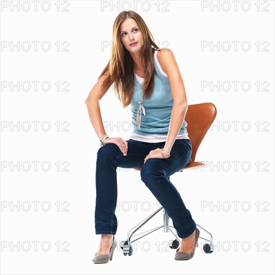 Studio shot of young woman sitting on chair with hands on laps. Photo : momentimages