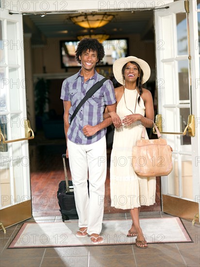 Couple exiting hotel with their luggage . Photo : db2stock