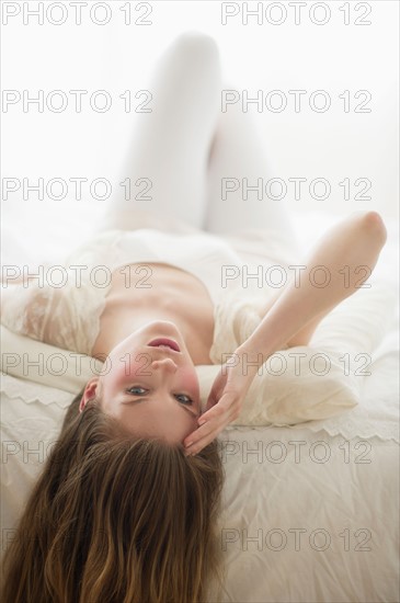 Studio portrait of young woman lying on bed.