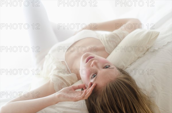 Studio portrait of young woman lying on bed.