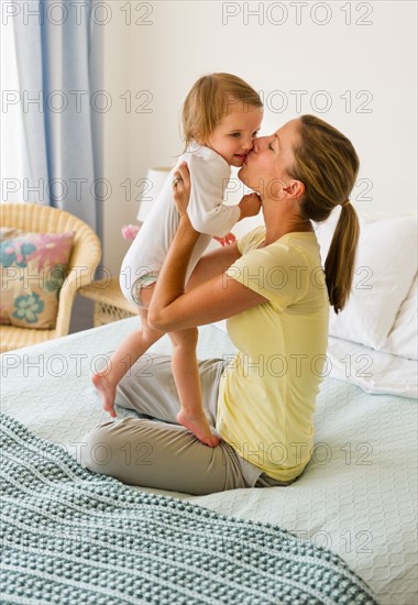 Mother kissing daughter (2-3) on bed.