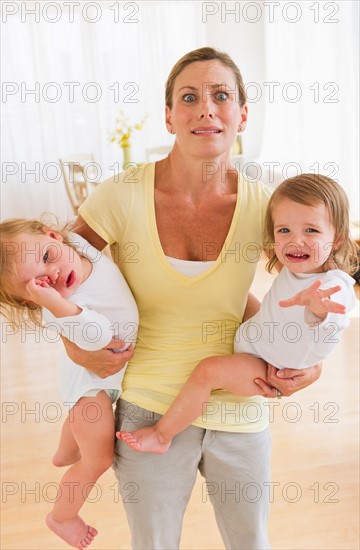 Mother holding crying daughters (2-3) and making facial expression.