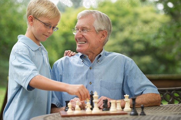 Grandfather and grandson (10-11) playing chess on porch.