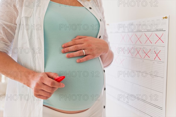 Young pregnant woman with marked calendar.