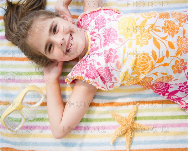 Smiling girl ( 6-7) lying on towel on vacations. Photo : Jamie Grill