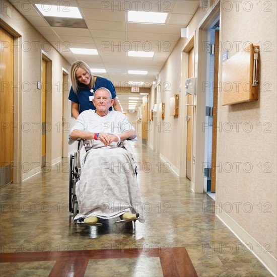 Young nurse is pushing senior man in wheelchair.