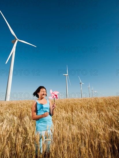 USA, Oregon, Wasco, Girl (10-11) holding fan in wheat field with wind turbines in background.