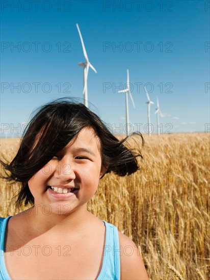 USA, Oregon, Wasco, Cheerful girl (10-11) standing in wheat field with wind turbines in background.