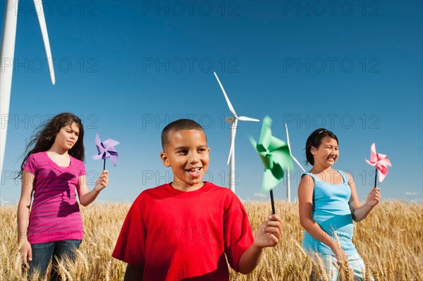 USA, Oregon, Wasco, Pre-teen girls (10-11) and boy (8-9) holding fans in wheat field in front of wind turbines.