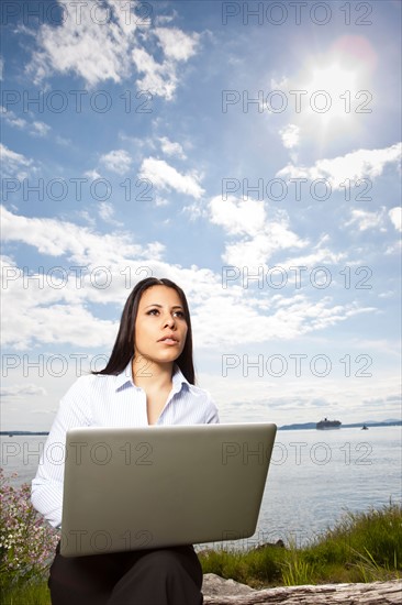 Young businesswoman using laptop on lakeshore. Photo: Take A Pix Media