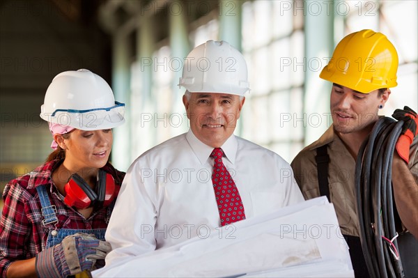 Portrait of manual workers and manager looking at blueprint. Photo : db2stock
