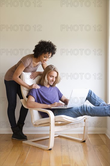 Young woman looking at man using laptop at home. Photo : Rob Lewine