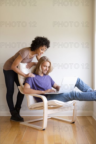 Young woman looking at man using laptop at home. Photo : Rob Lewine