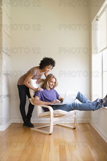 Young woman looking at man using laptop at home. Photo : Rob Lewine